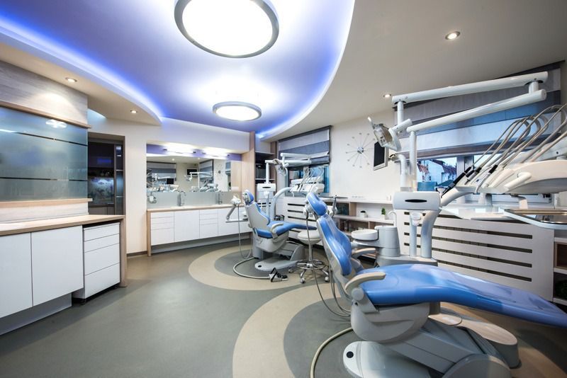 Modern dental office with blue chairs and equipment, neutral tones, and curved ceiling lighting.