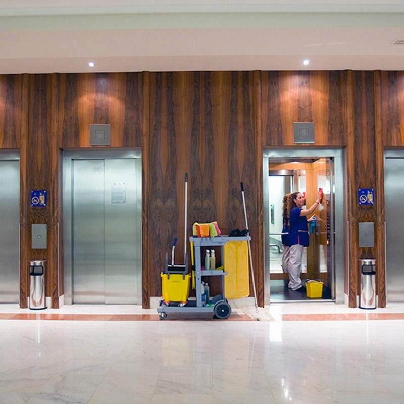 Elevator lobby with a cleaning cart and person cleaning an open elevator.