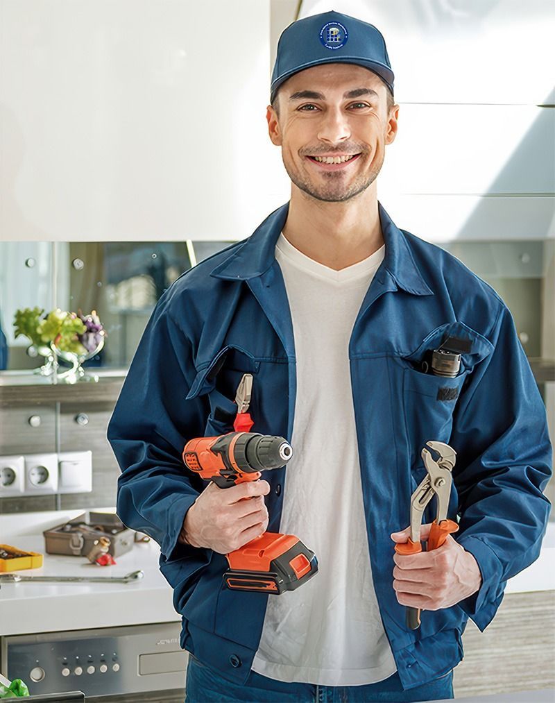 Handyman holding a drill and pliers, smiling in a kitchen wearing a blue uniform and cap.