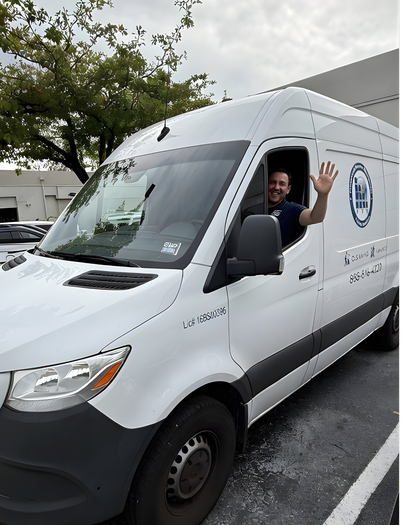 Man waves from the driver's seat of a white van with company logo parked outside.