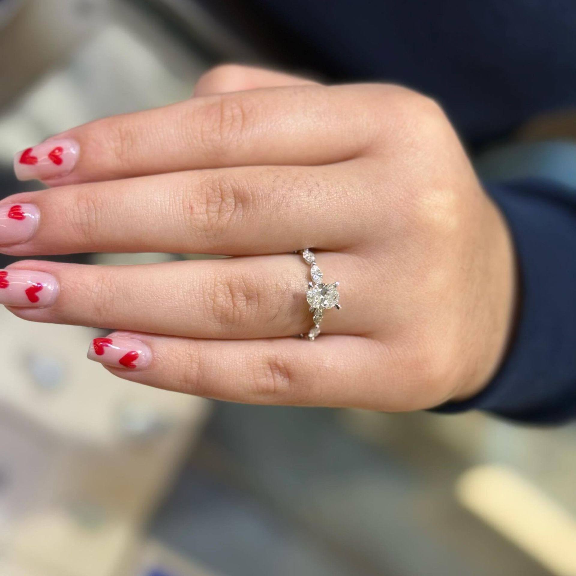 Hand with a diamond ring and red heart nail art.