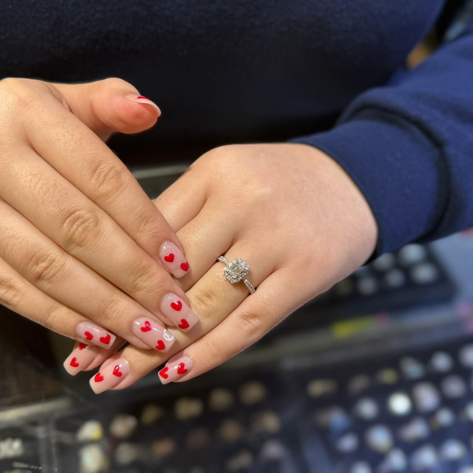 Person's hands with heart-decorated nails and diamond ring.