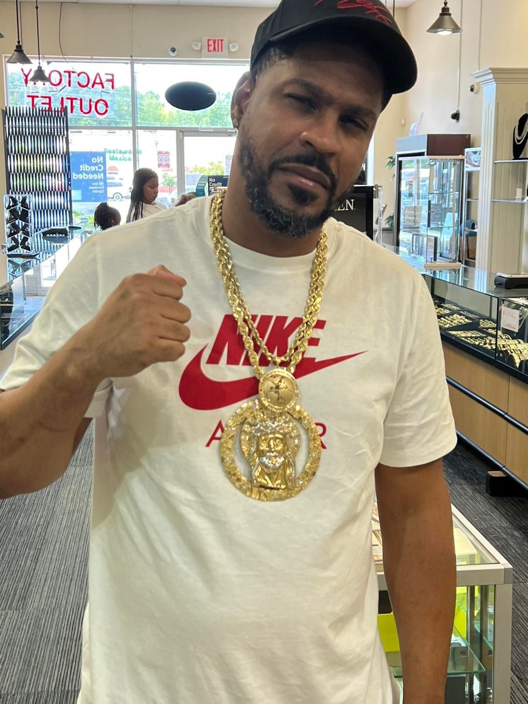 Man wearing gold chain and Nike shirt, inside a jewelry store. He is clenching his fist.