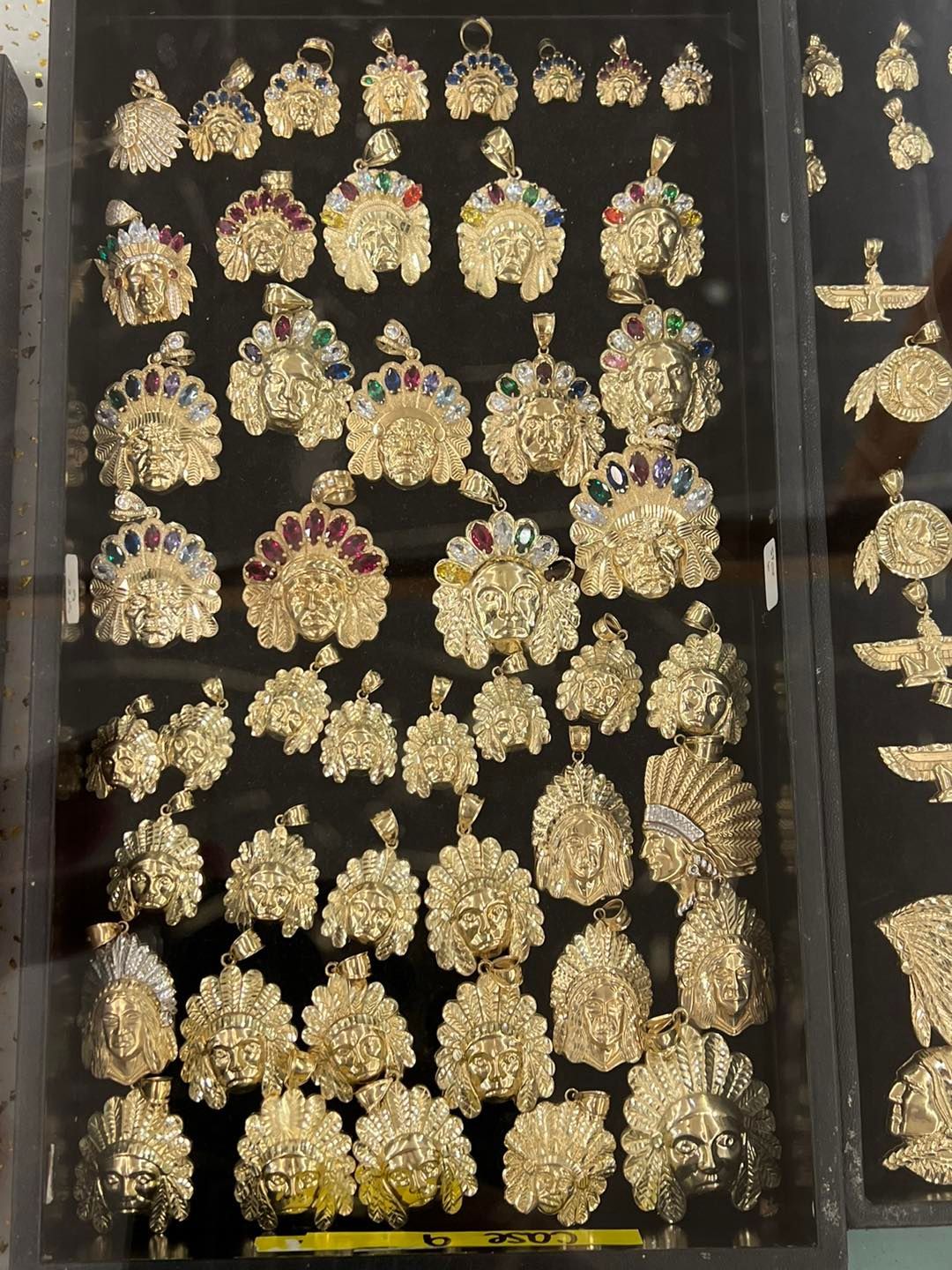 Gold pendants in a display case. Many are adorned with colorful gemstones.