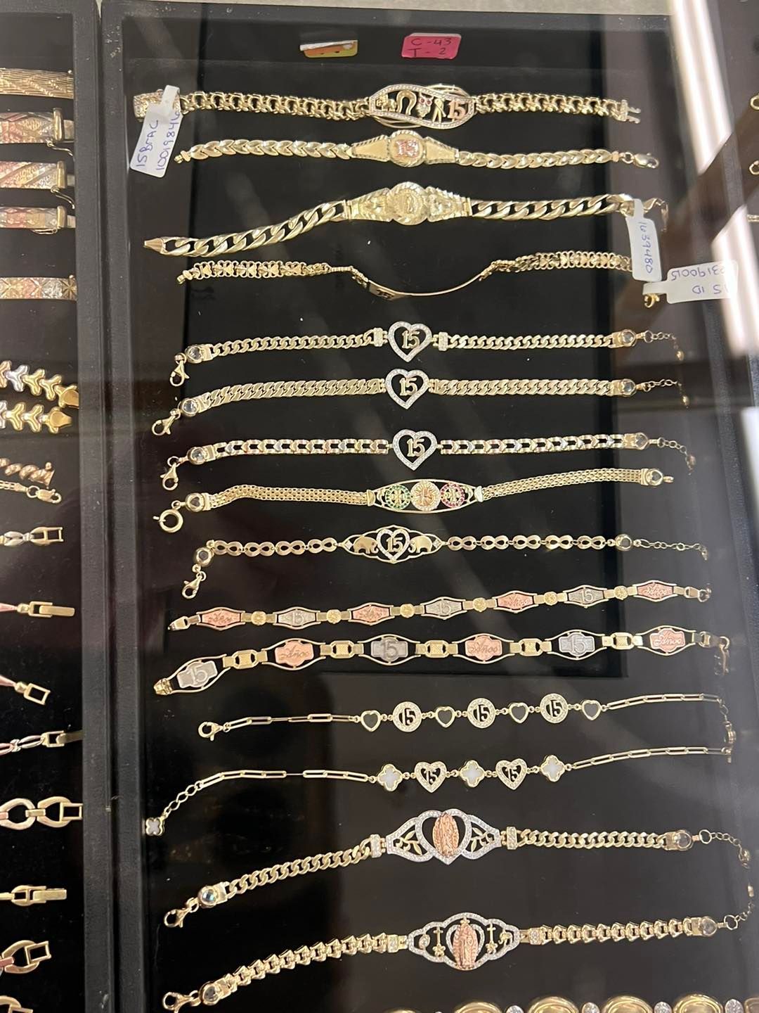 Gold bracelets displayed in a jewelry store case, various styles, including chain, charms, and initials.