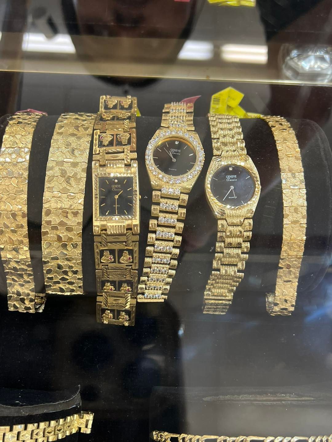 Gold watches and bracelets in a display case. Black faces, diamond accents, and textured gold bands.
