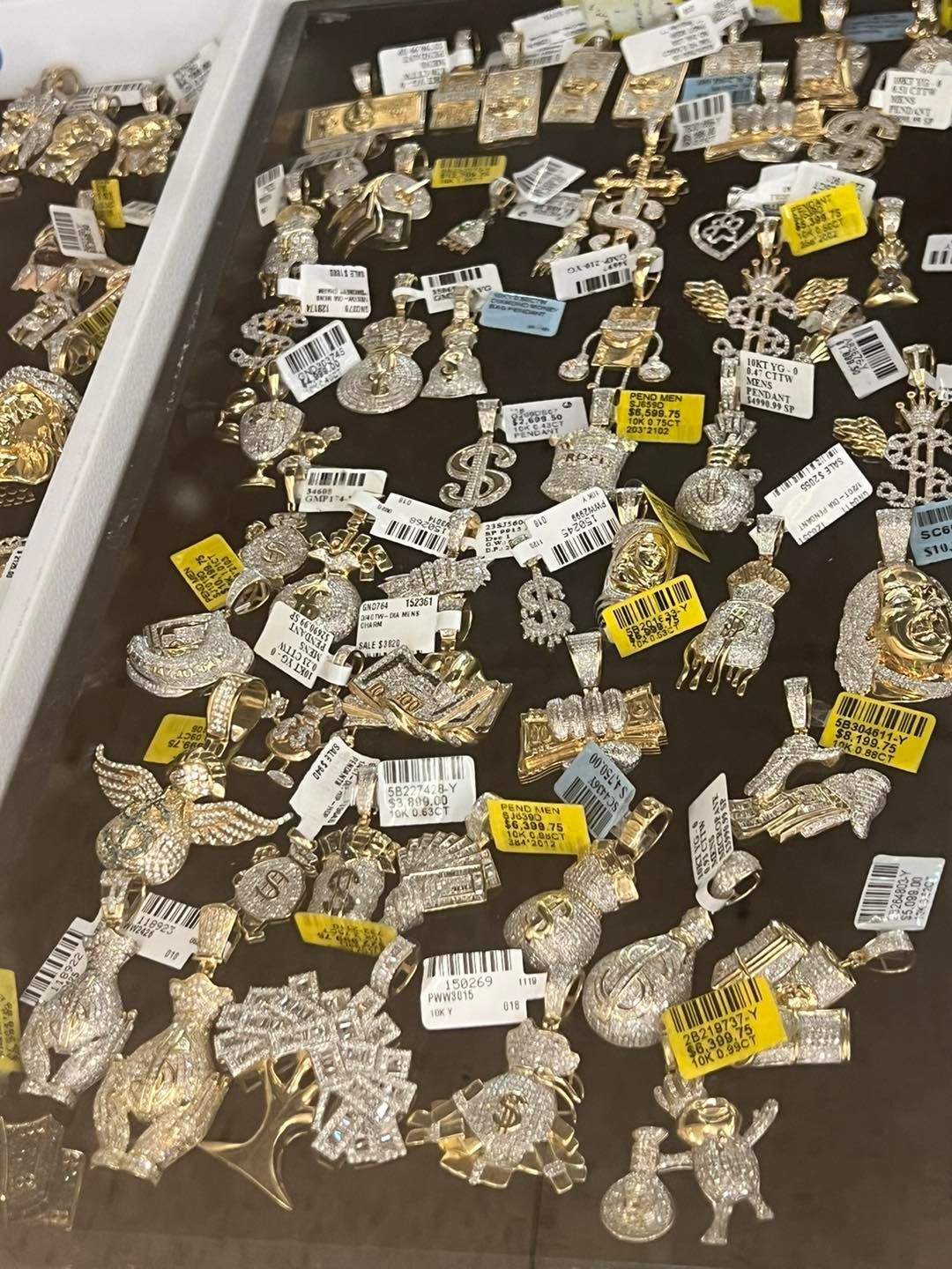Jewelry display case with numerous gold and diamond pendants with price tags.