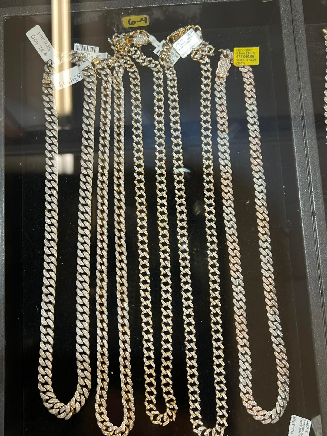 Cuban link chain necklaces displayed in a jewelry case. Gold color, various lengths, price tags attached.