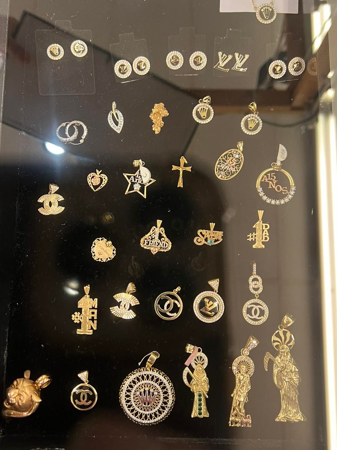 Jewelry display: gold pendants with various designs including crosses, logos, and figures.