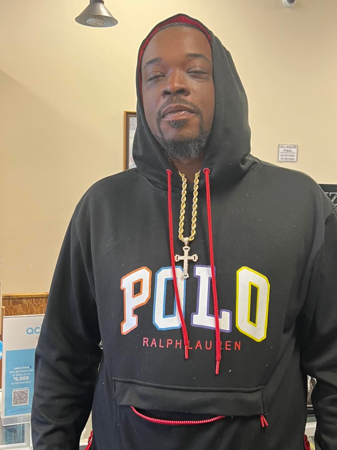 Man in black Polo hoodie with gold chain, standing indoors.
