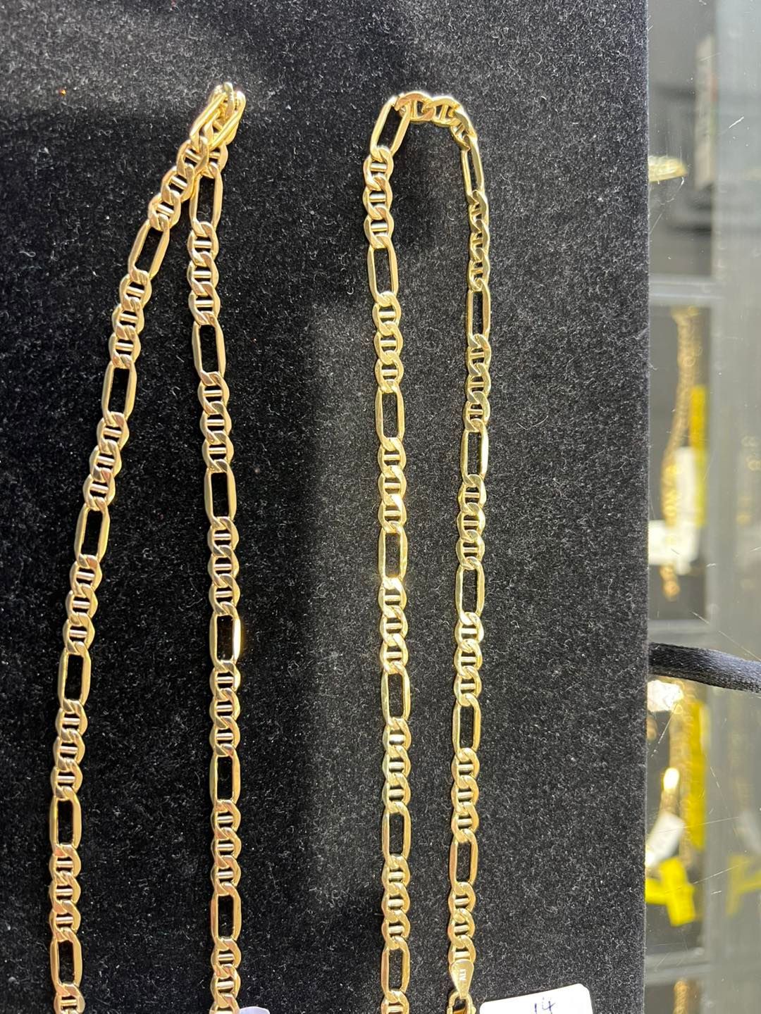 Two gold mariner link chains on a black velvet display.