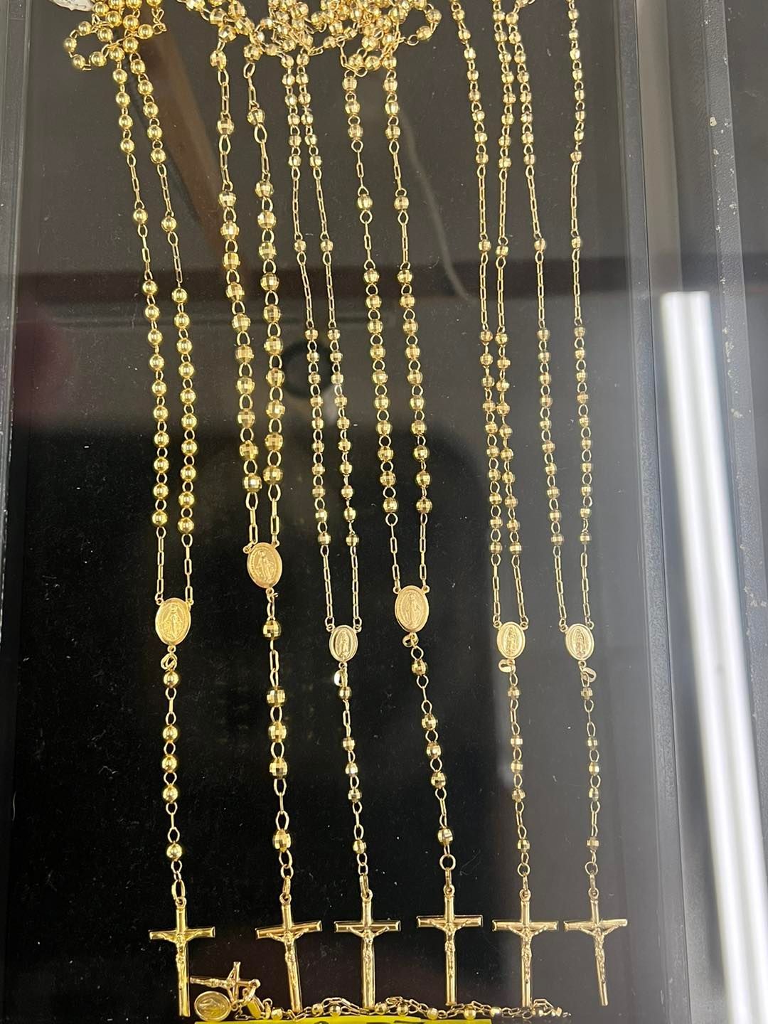 Gold rosary necklaces displayed inside a showcase.