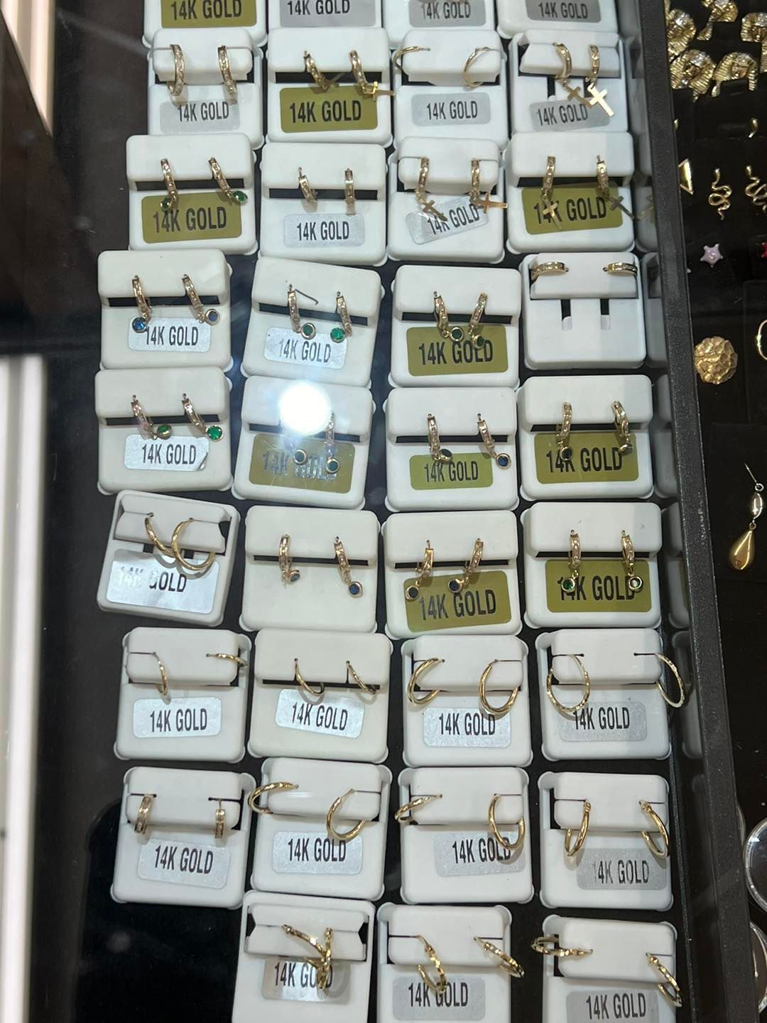 Rows of small white boxes filled with various gold hoop earrings, displayed in a jewelry case.