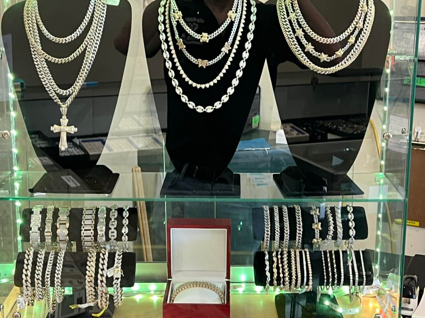 Jewelry display case with necklaces and bracelets on black velvet stands. Silver and white pieces.
