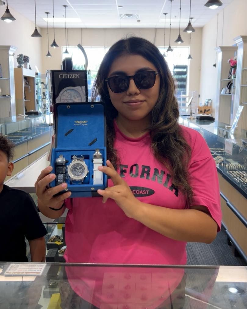 Woman in sunglasses holding a watch box inside a jewelry store. She wears a pink shirt and smiles.