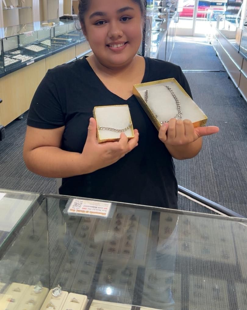 Woman in jewelry store smiling, holding two jewelry boxes with necklaces.