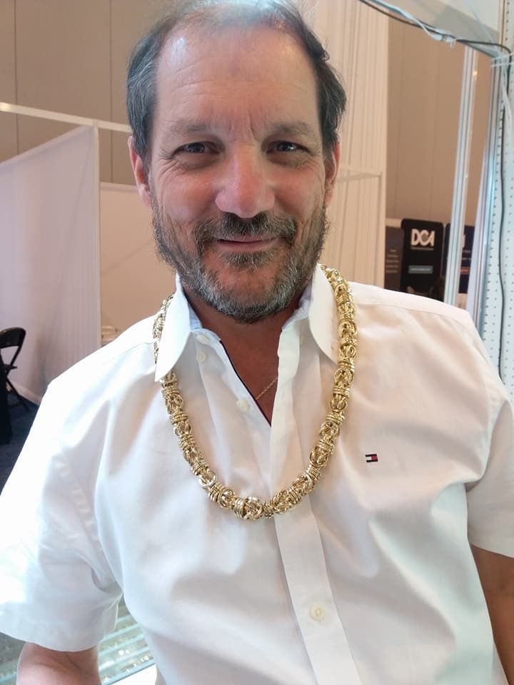 Man wearing a gold chain and white shirt, smiling.