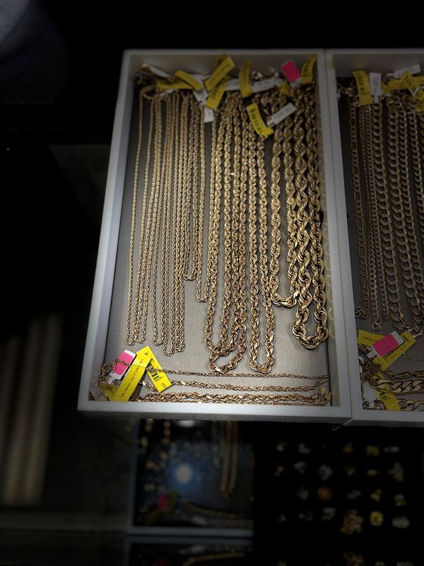 Gold chains displayed in a jewelry store case, each tagged with price information.