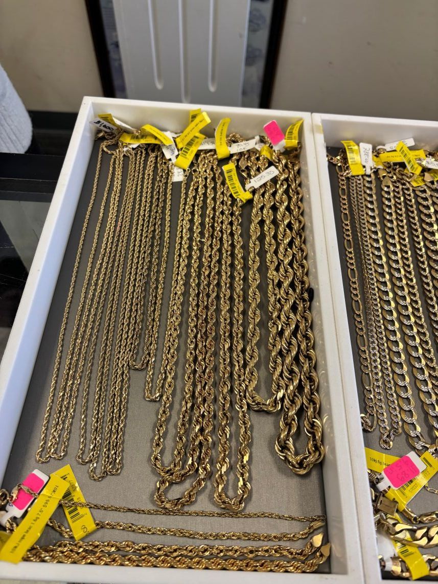 Gold necklaces in a jewelry display case, various styles, yellow price tags.