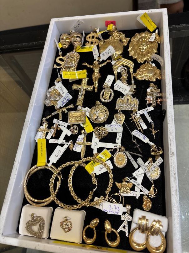 Gold jewelry displayed on black velvet in a white tray. Pendants, earrings, and bracelets. Yellow price tags.