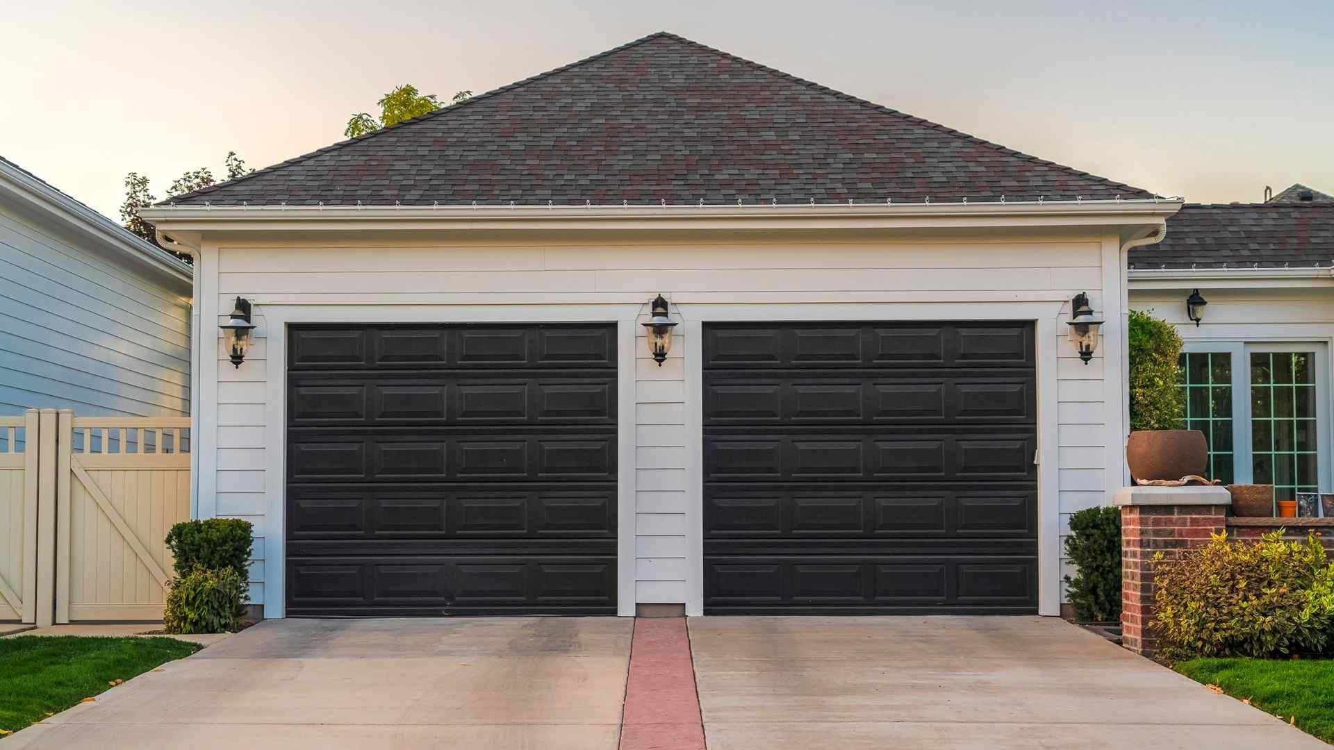 White house with two black garage doors and a brick driveway.