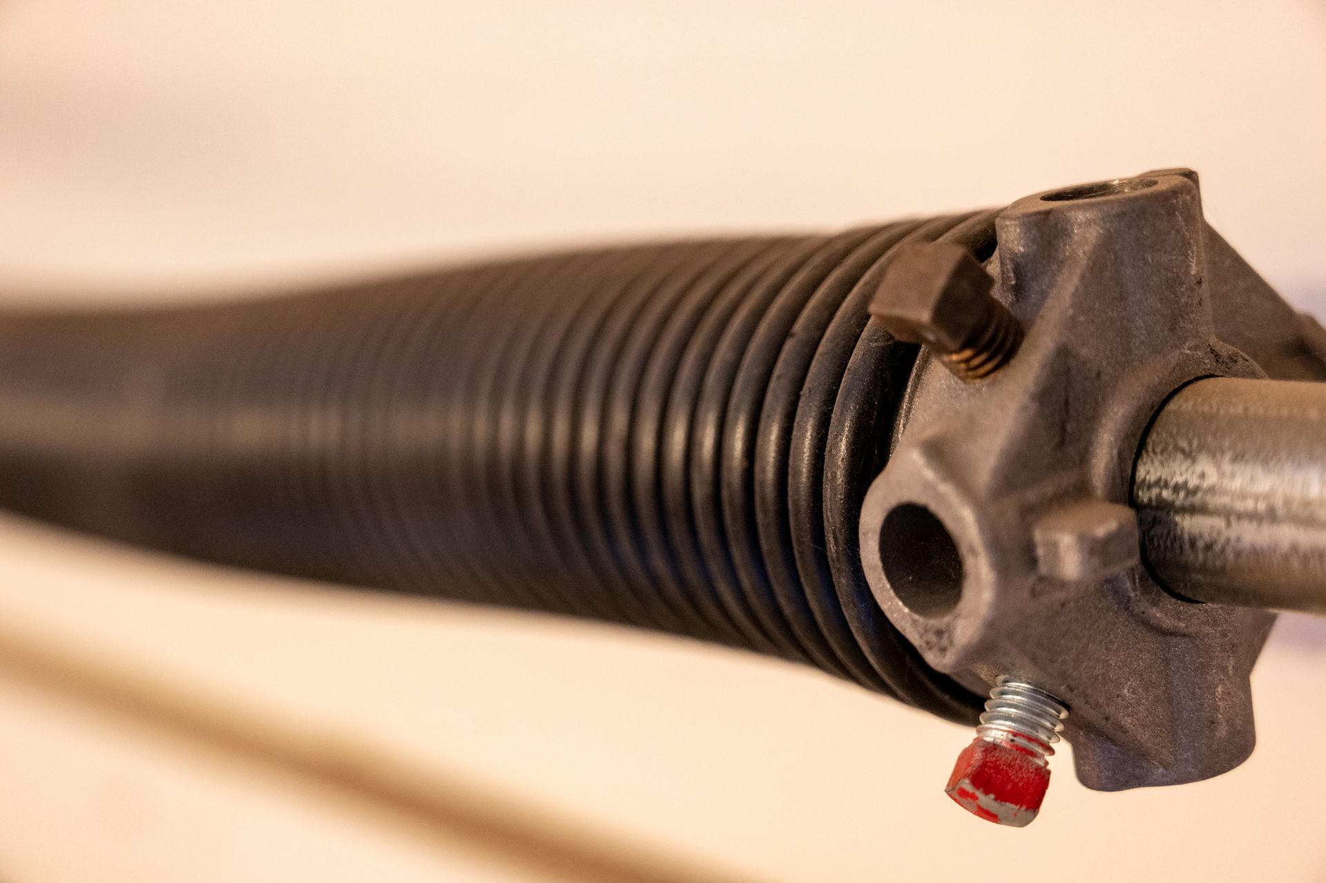 Close-up of a black garage door torsion spring with a metal end piece and red-capped bolt.