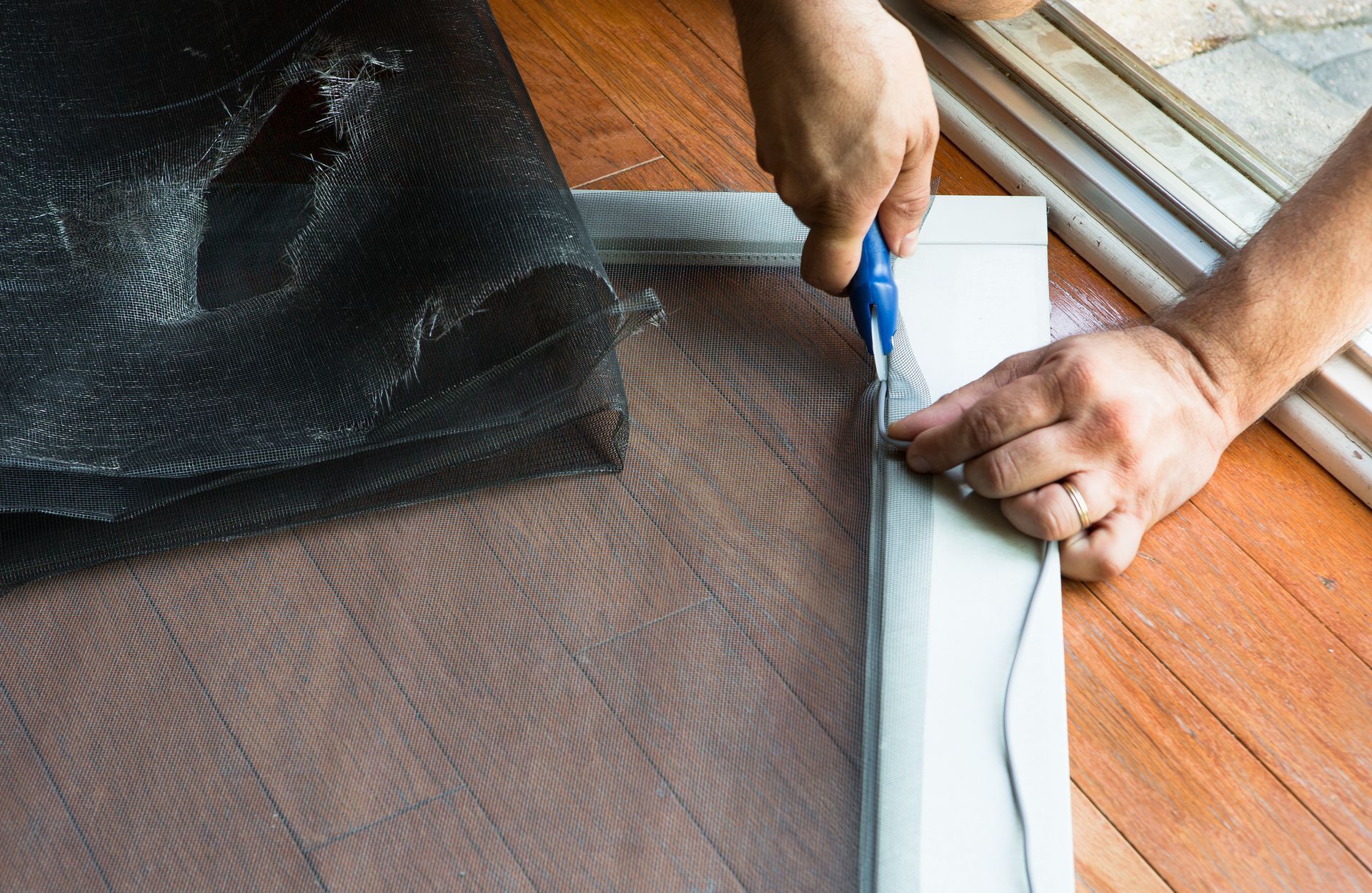 Person trimming excess screen material from a screen frame with a utility knife.