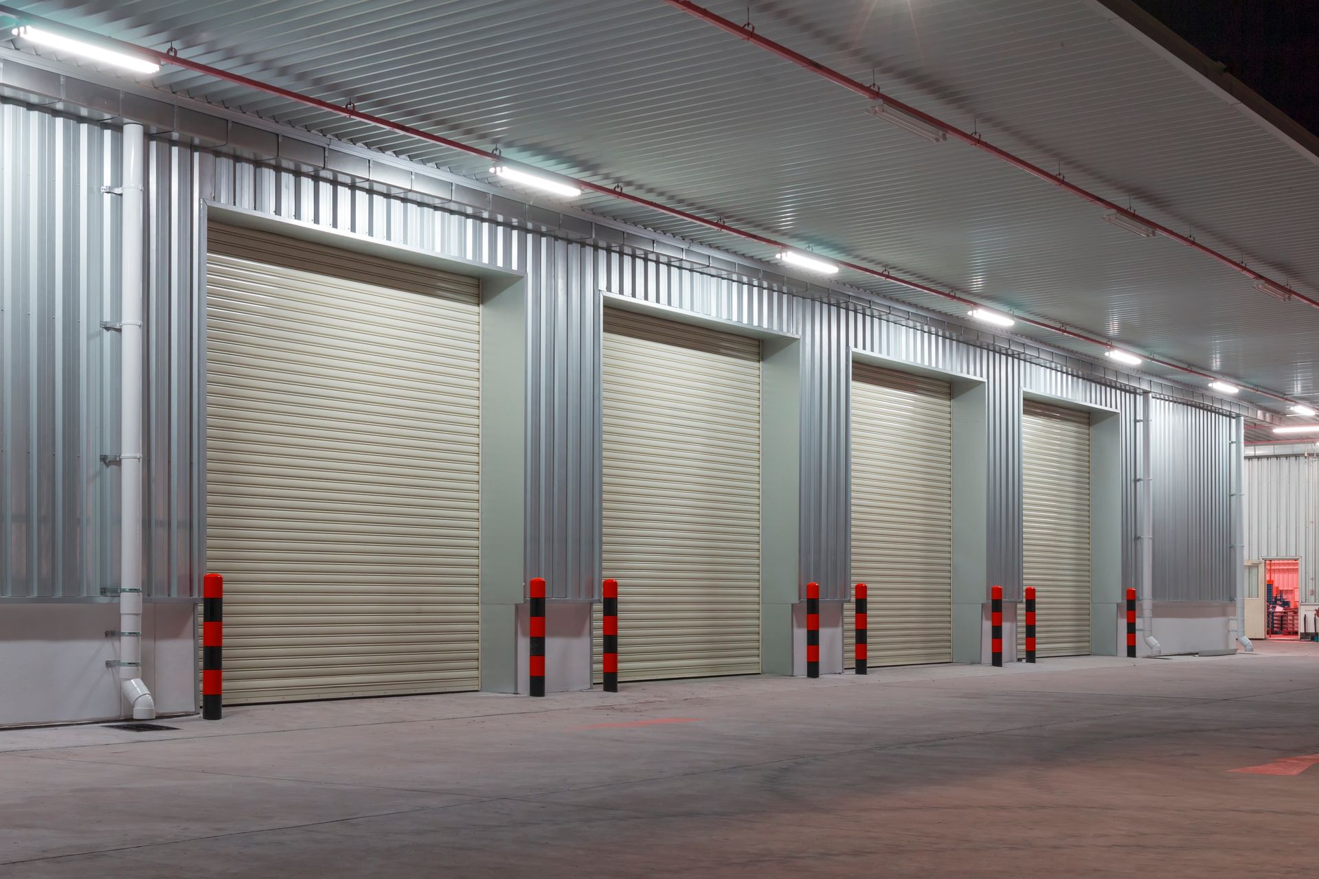 Four beige roller doors on a corrugated metal building, illuminated by overhead lights.