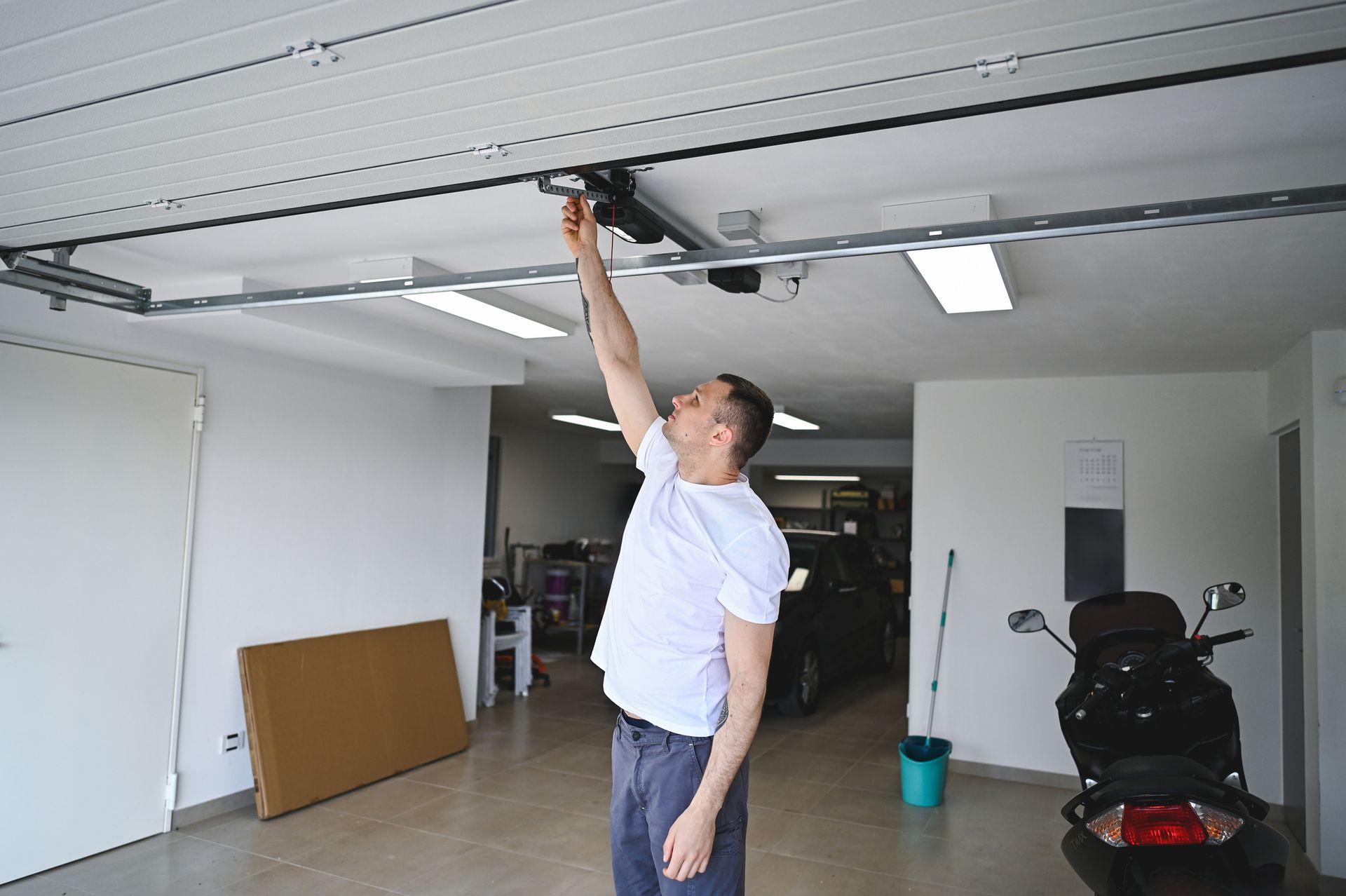 Man reaching up to adjust garage door opener in a white garage.