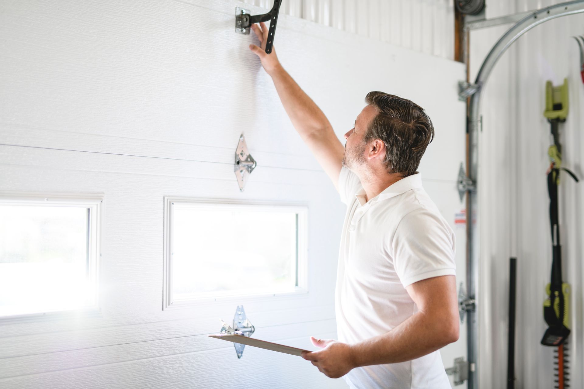 Man in white shirt inspecting garage door, holding clipboard.
