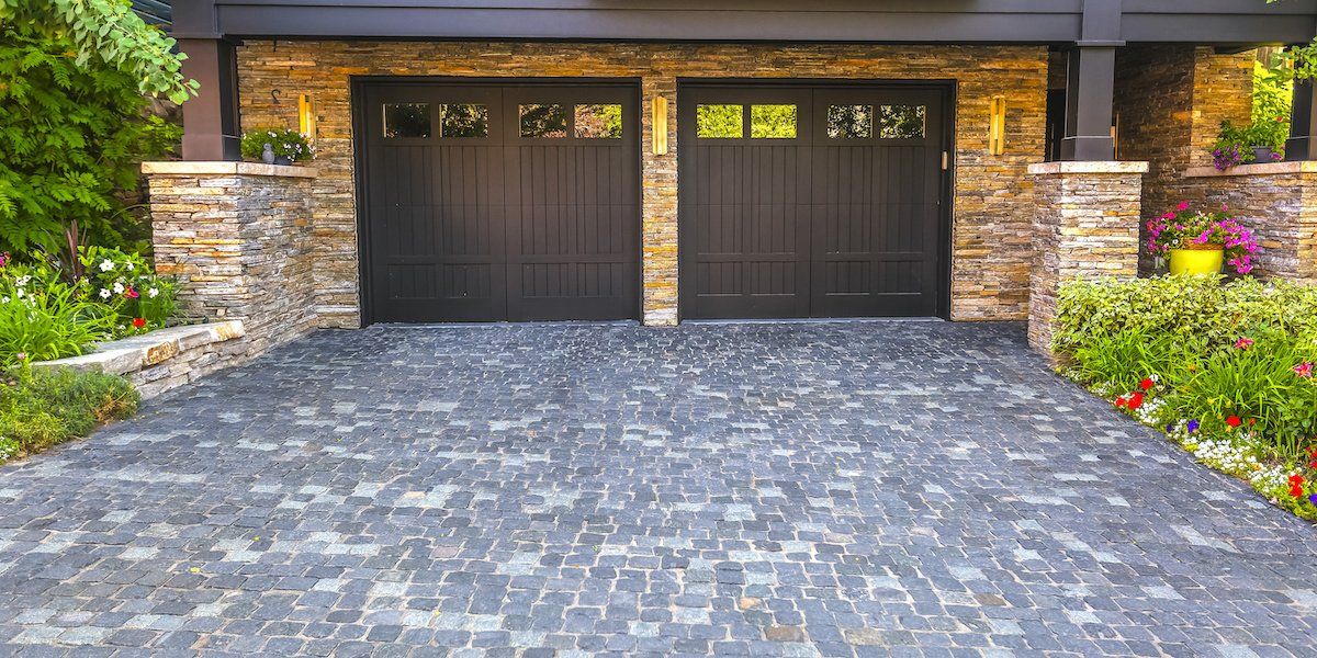 There is a driveway leading to a garage with two black garage doors.