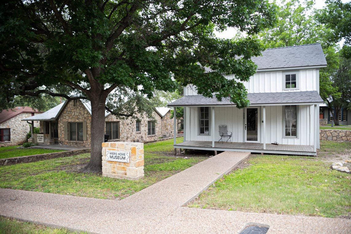 A white house with a porch and a tree in front of it.