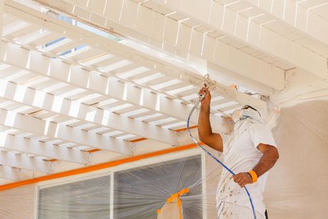man wearing mask while painting the ceiling using a spray paint