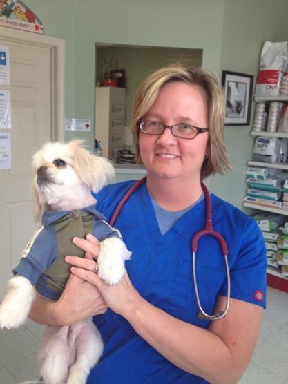 A woman in a blue scrub is holding a small white dog