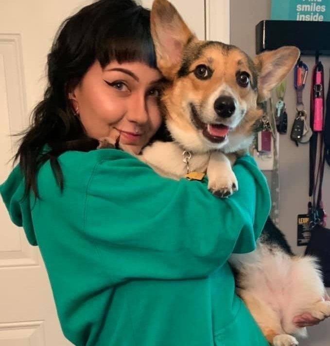 A woman in a green hoodie is holding a brown and white dog