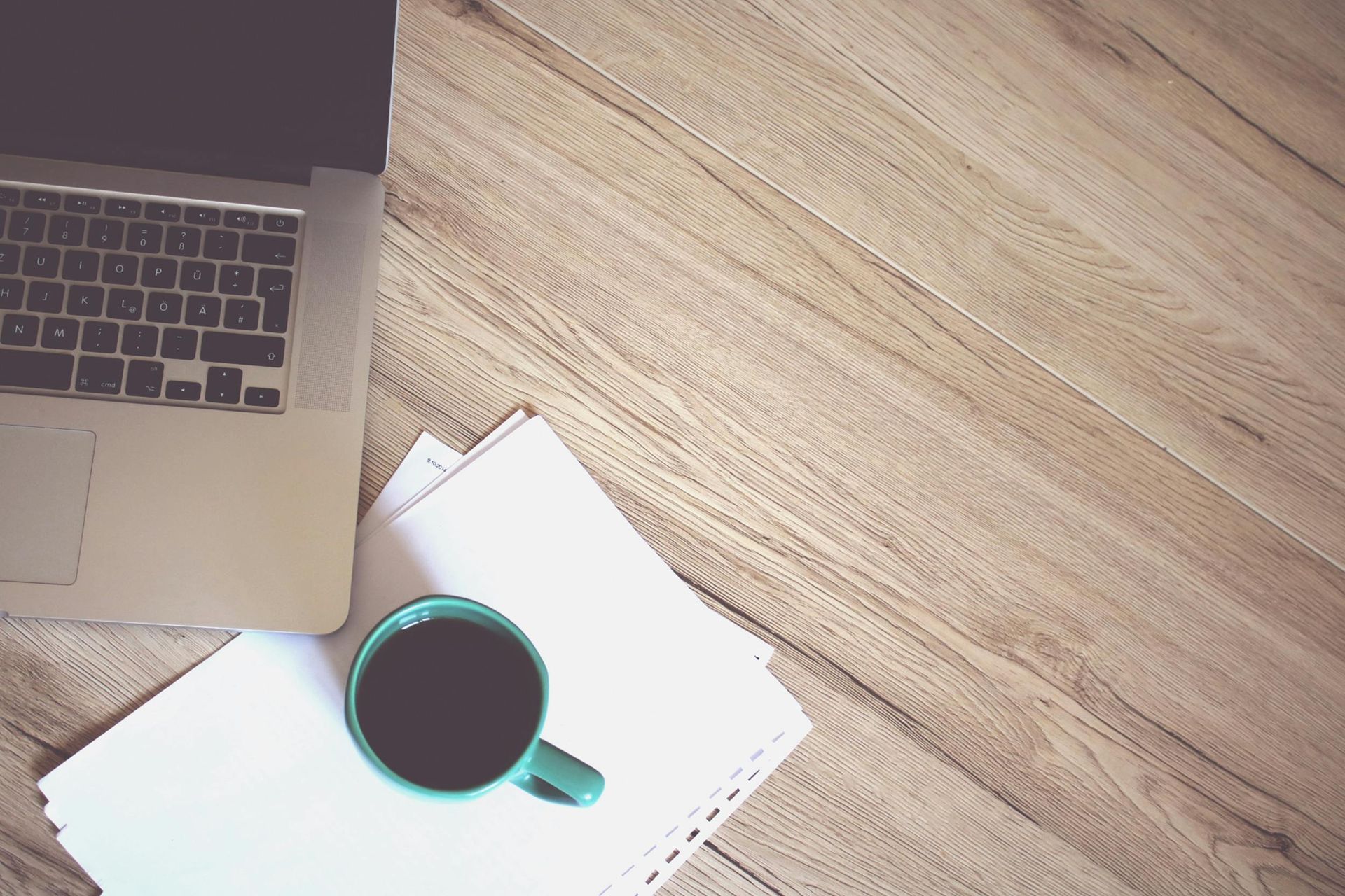 A cup of coffee and a laptop are on a wooden table.