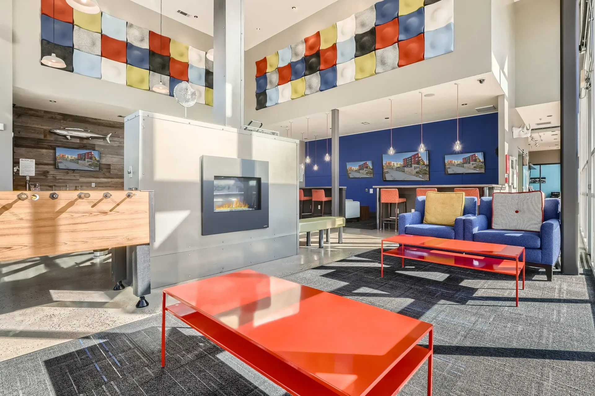 Modern apartment community lounge with colorful wall art, seating, and a fireplace.