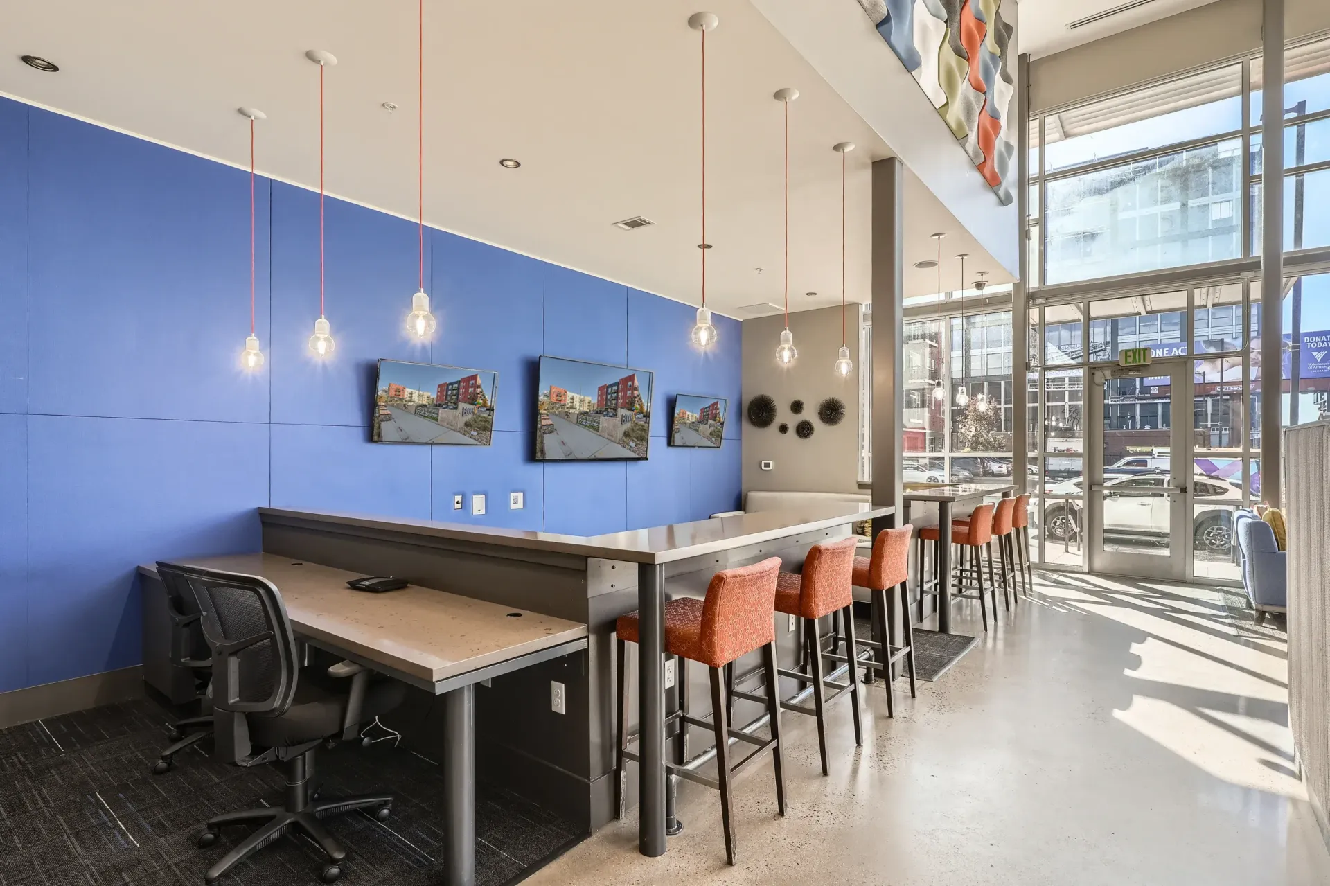 Modern lobby with a blue accent wall, a long countertop with orange bar stools, hanging pendant lights, and a glass entry.