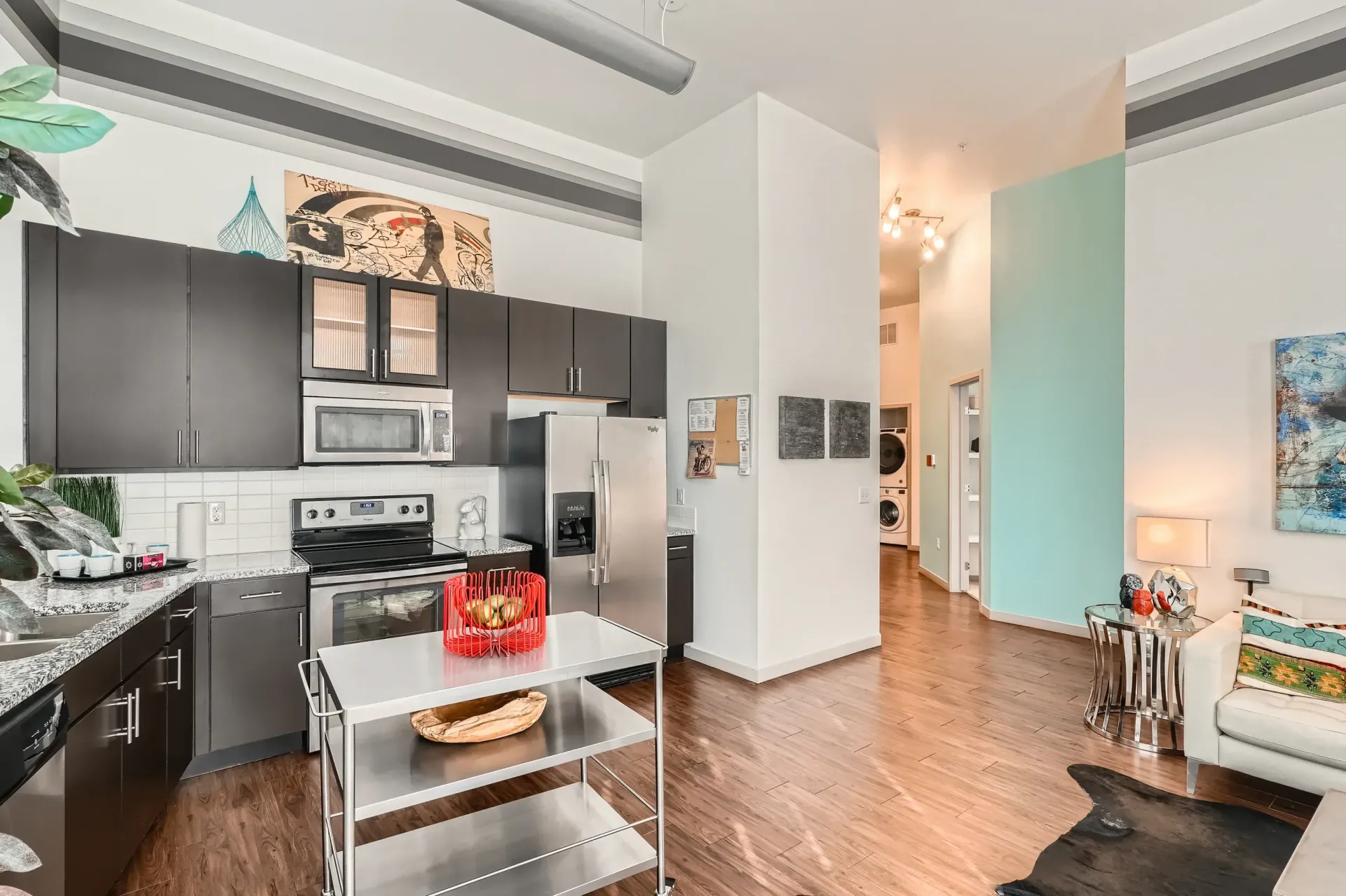 Open-concept kitchen with dark cabinets, stainless appliances, and a metal island in a modern living space.