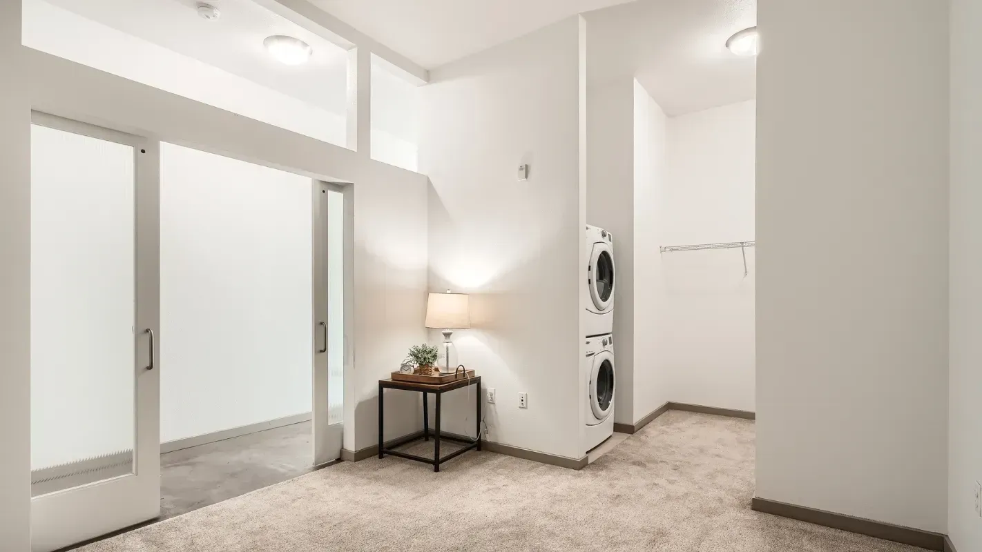 Interior laundry area with stacked washer and dryer beside a small table and lamp.