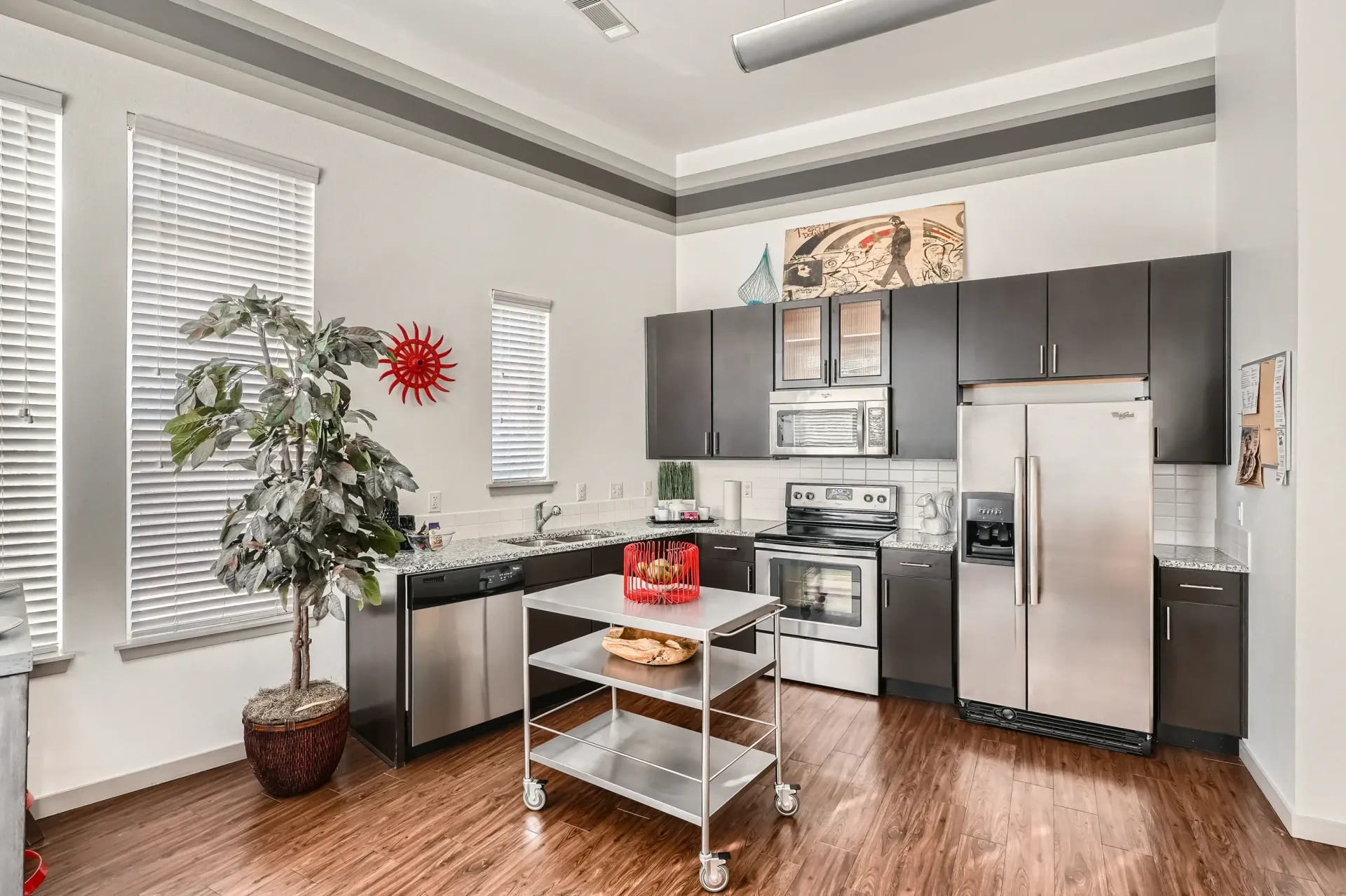Modern apartment kitchen with dark cabinets, stainless appliances, and a rolling cart.