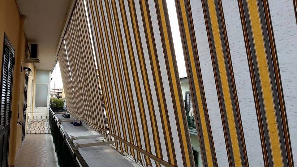 Un balcone con una tenda da sole a strisce gialle e bianche.