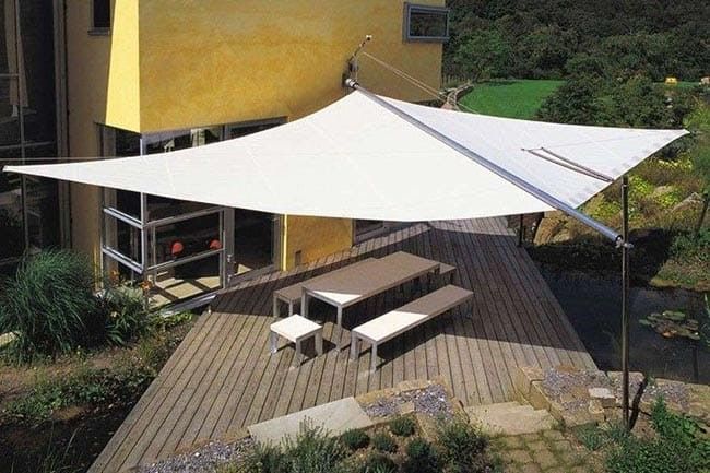 Un grande ombrellone bianco copre una terrazza di legno con un tavolo e delle panche.