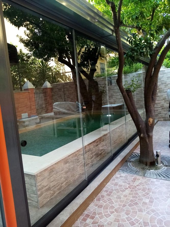 Una piscina è dietro una parete di vetro con un albero sullo sfondo.