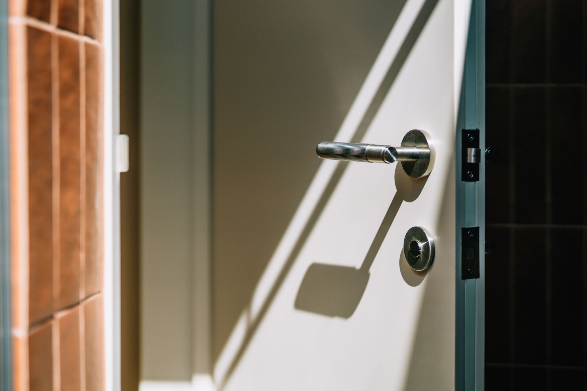 Sunlit modern door handle on partially open white door with shadows, photo by Oscar Wong