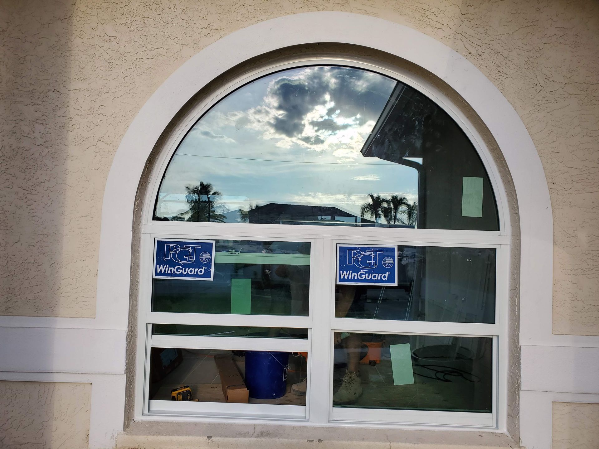 Arched window on tan stucco wall, reflecting sky and building. Two blue 