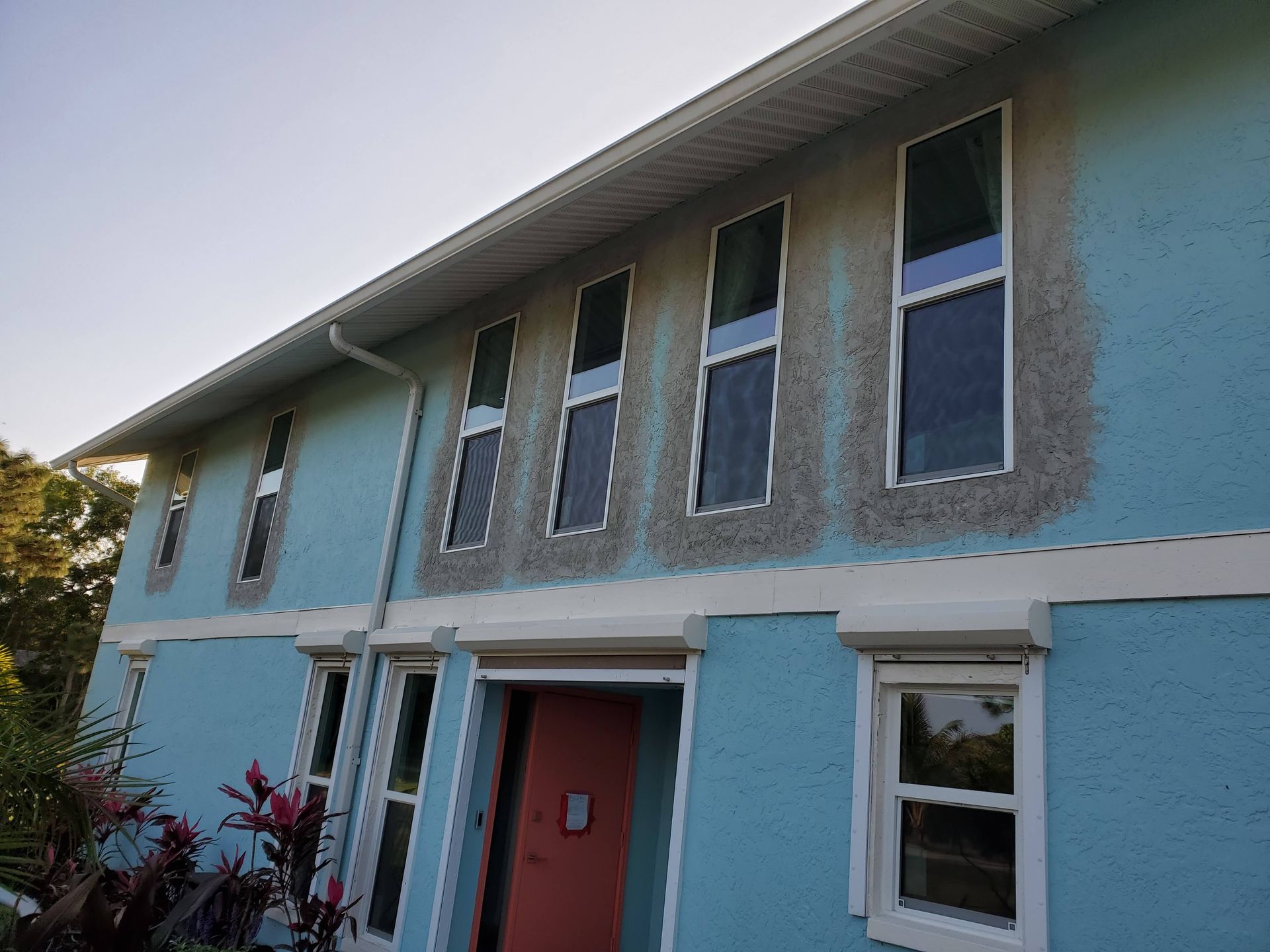 A blue two-story house with window outlines in gray. The front door is coral.