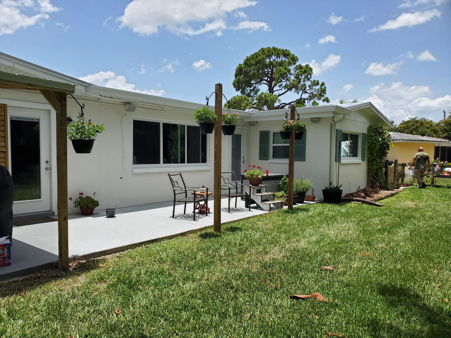 White house with gray patio, outdoor seating, and hanging plants on a sunny day.