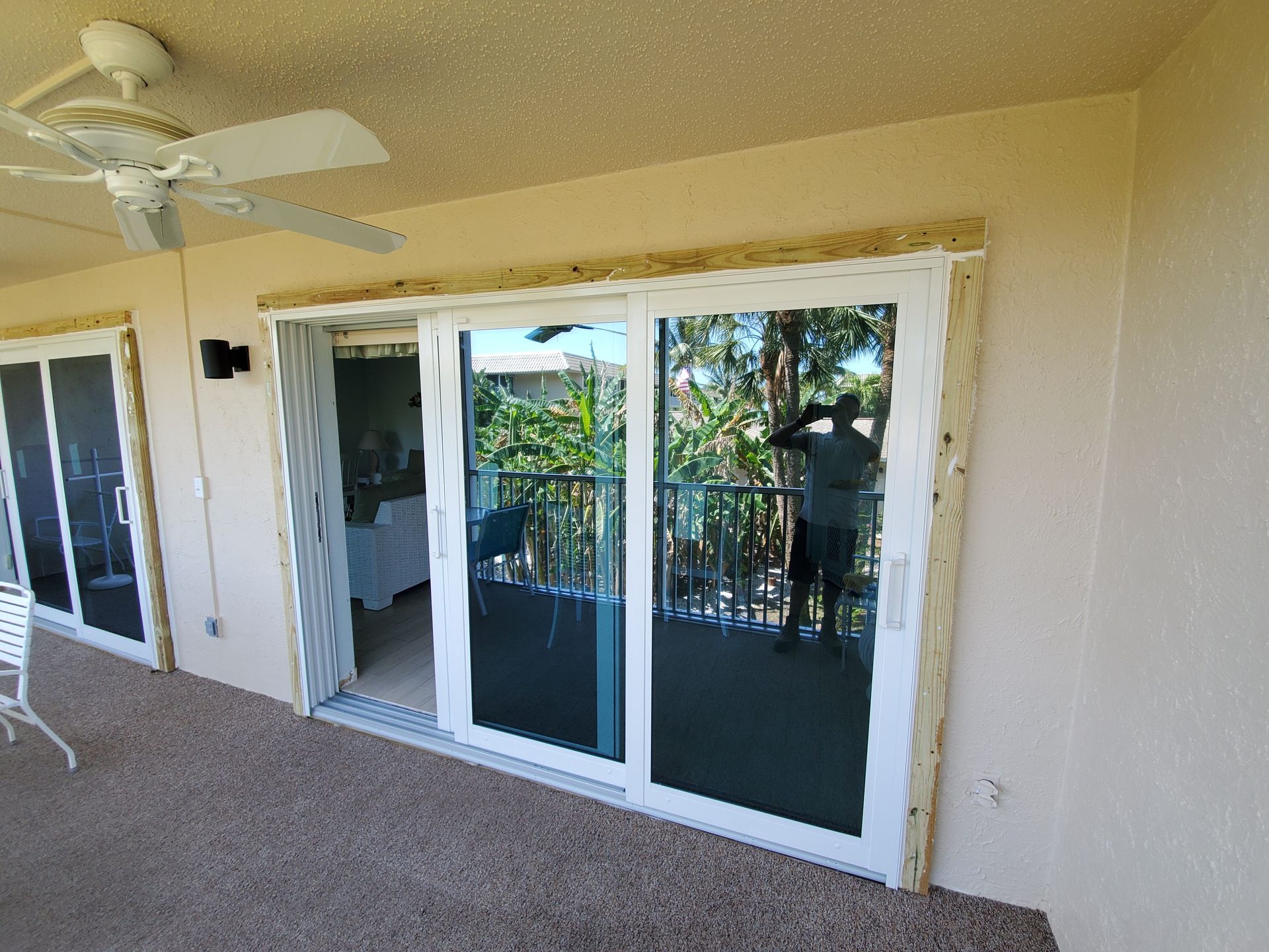 A sliding glass door with white trim, reflecting a balcony with a person, trees, and a beige exterior.