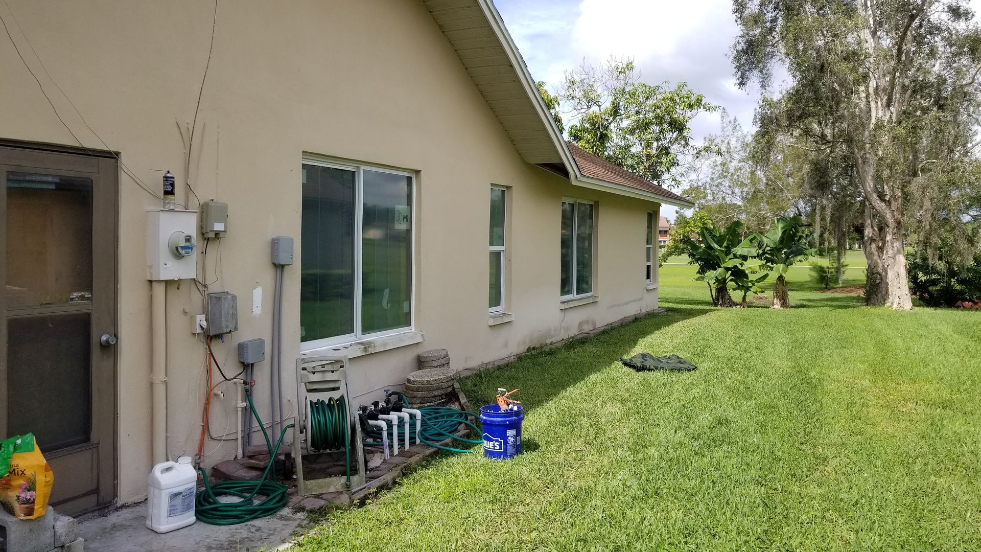 Beige house exterior with windows and yard, equipment and tree.